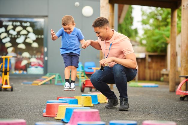 Nursery teacher helping young child to jump