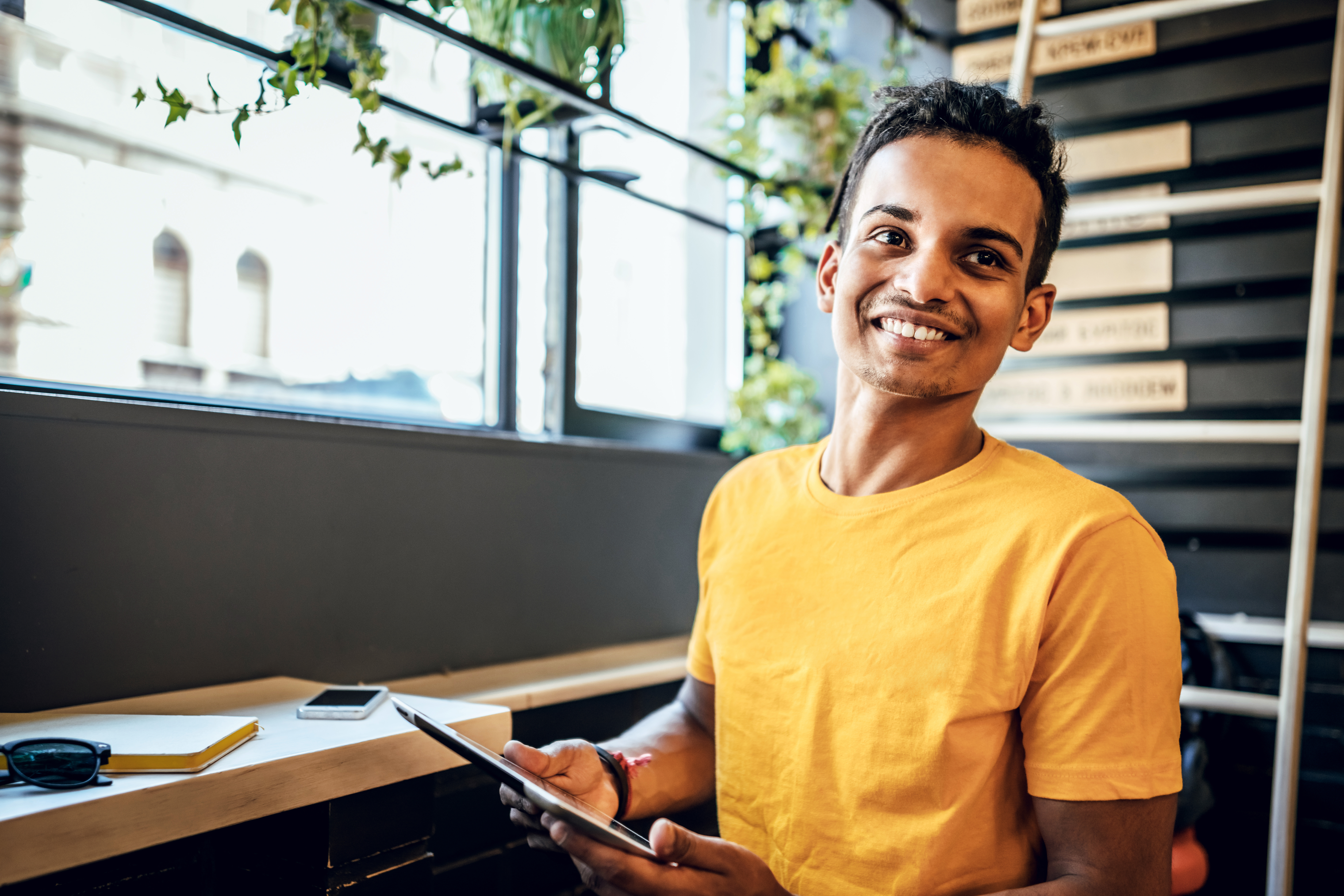 1343350871 young man smiling in a mustard yellow crew neck shirt holding a tablet